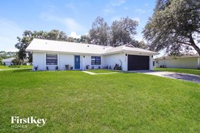 Palm Bay house for rent - A white house with a black garage door is surrounded by a grassy lawn.