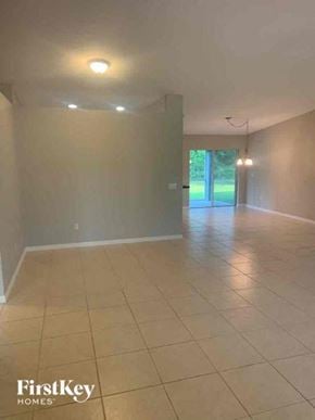 North Port house for rent - A spacious room with tiled flooring and a view of a green outdoor area through a glass door.