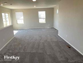 Commerce City house for rent - an empty living room with gray carpet and two windows