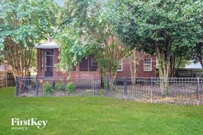 Murfreesboro house for rent - A brick house with a fence and trees in front of it.