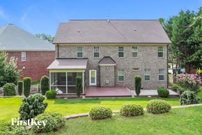 Winston Salem house for rent - A house with a red brick exterior and a grey roof is surrounded by a well-manicured lawn and a variety of shrubs.