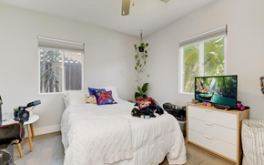San Diego apartment for rent - A bedroom with a bed, a desk with a chair, and a window with a view of a tree.