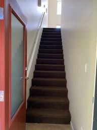 Nanaimo apartment for rent - A brown carpeted staircase with a red door on the left.