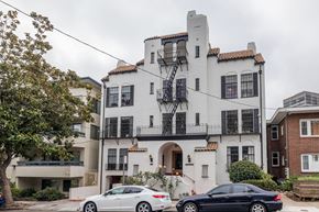 Oakland apartment for rent - A white building with a black balcony and a car parked in front.