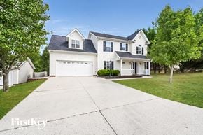High Point house for rent - A large white house with a black roof and a garage is surrounded by trees.