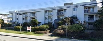 Coquitlam apartment for rent - A white apartment building with balconies and bushes in front.