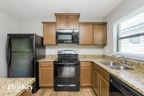 Wimauma house for rent - A kitchen with a black refrigerator, black stove, and wooden cabinets.