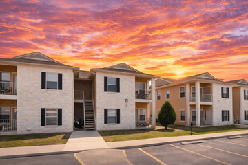 Kerrville apartment for rent - A sunset view of apartment buildings with a parking lot in the foreground.