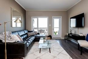 Saskatoon apartment for rent - A living room with a black leather couch, a glass coffee table, and a flat-screen TV mounted on the wall.