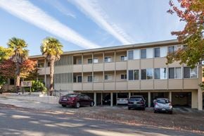 Oakland apartment for rent - A parking lot with cars and a building with palm trees in front.