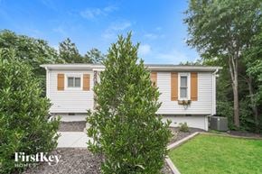 Charlotte house for rent - A white house with brown shutters is surrounded by greenery.