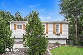 Charlotte house for rent - A white house with brown shutters is surrounded by greenery.