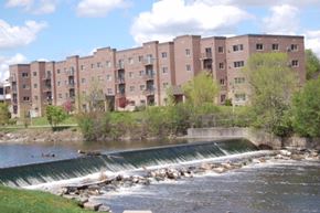 West Bend apartment for rent - A river flows past a dam and apartment buildings.