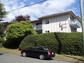 Nanaimo apartment for rent - A black car is parked on the side of a road in front of a white house with a hedge.