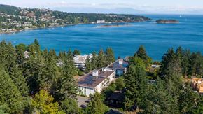 Nanaimo apartment for rent - A large white building with a black roof is surrounded by trees.