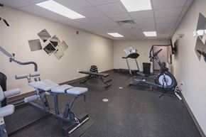 Watford City apartment for rent - A gym room with a variety of equipment including a rowing machine, a leg press machine, and a bench press.