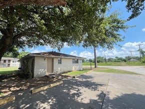 Bay City house for rent - A small building with a brown door is surrounded by a tree and a grassy area.