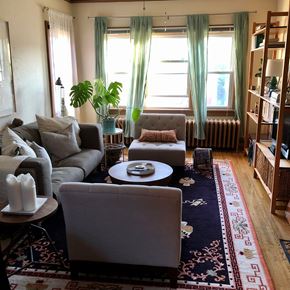 Minneapolis apartment for rent - A living room with a grey couch, a round table, and a large window with curtains.