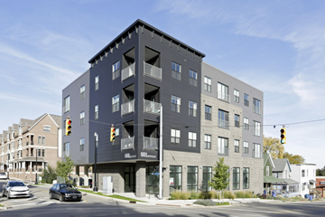Grand Rapids apartment for rent - A modern multi-story building with a black facade is situated on a street corner with cars and traffic lights visible.