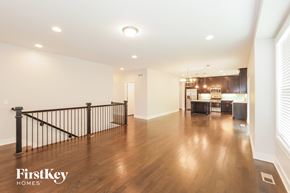 Raymore house for rent - A spacious room with wooden floors and a black railing.