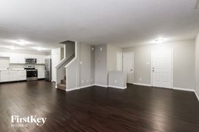 Indianapolis house for rent - A spacious room with wooden floors and white walls, featuring a staircase and a kitchen area.