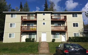 Wasilla apartment for rent - A black car is parked in front of a tan apartment building.