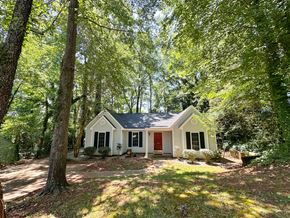 Clemson house for rent - A small white house with a red door is surrounded by trees.
