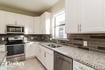 Alva house for rent - a kitchen with white cabinets and granite counter tops and a sink