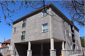 Oshawa apartment for rent - A grey stone building with a balcony and a tree branch in the foreground.