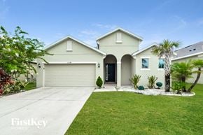 Kissimmee house for rent - a beige house with a lawn and palm trees