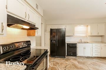 Lenexa house for rent - a kitchen with white cabinets and black appliances