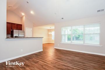 Charlotte house for rent - A spacious room with wooden floors and a kitchen area with a refrigerator and cabinets.