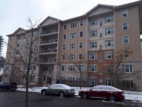 Waterloo apartment for rent - Two cars are parked in a parking lot in front of a large apartment building.