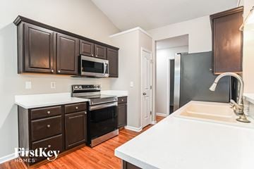 Charlotte house for rent - a kitchen with dark wood cabinets and white countertops and a sink and a microwave
