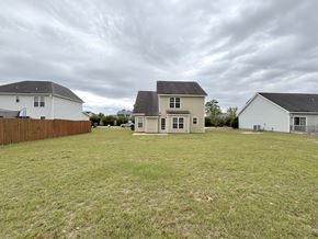 Hope Mills house for rent - A large grassy field with two houses and a fence in the background.