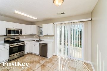 Austell house for rent - A kitchen with white cabinets and appliances, a tiled floor, and a sliding glass door.