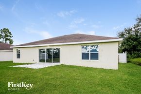 Lehigh Acres house for rent - the front view of a white house with a grassy yard and a patio