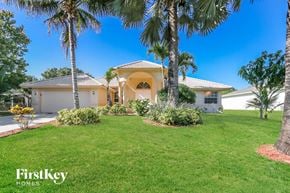 Port St. Lucie house for rent - A house with a white exterior and a yellow roof is surrounded by greenery and palm trees.