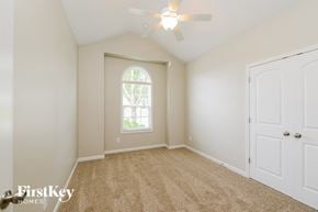Winston Salem house for rent - A room with a carpeted floor, a ceiling fan, and a window with a view of trees.
