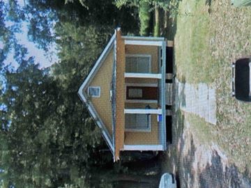 Hattiesburg house for rent - A small house with a brown roof and a white door is surrounded by trees.