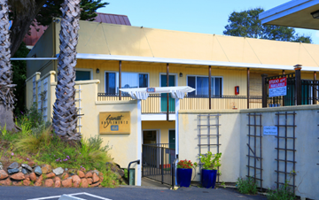 Mill Valley apartment for rent - the front of a yellow motel building with a gate and a palm tree