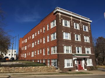 Tulsa apartment for rent - A red brick building with a green roof and a black fence in front.