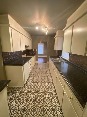 Tulsa house for rent - a kitchen with white cabinets and black counters and a tiled floor