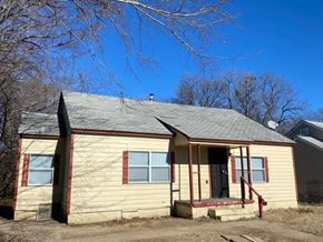 Tulsa house for rent - A small house with a porch and a door is surrounded by bare trees.
