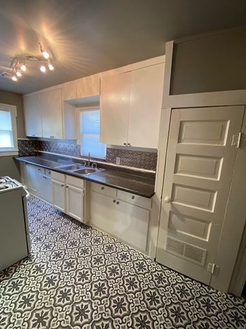 Tulsa house for rent - an empty kitchen with white cabinets and a white door
