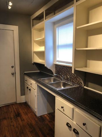 Tulsa house for rent - a kitchen with white cabinets and a sink and a window