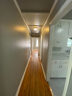 Tulsa house for rent - A long hallway with white walls and wood floors leads to a kitchen area.