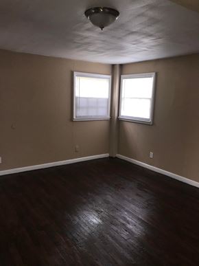 Tulsa house for rent - an empty living room with wood floors and two windows