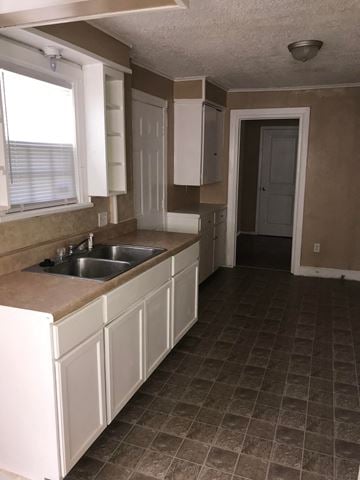 Tulsa house for rent - an empty kitchen with white cabinets and a sink