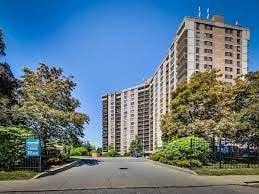 Etobicoke apartment for rent - A tall residential building is surrounded by trees and a street in front.